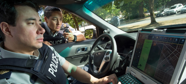 officers checking police database on laptop in police car